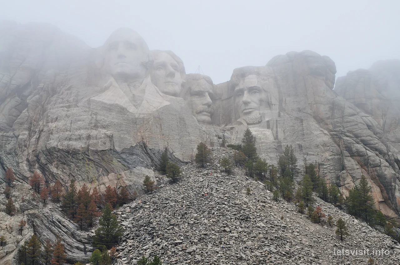 Mount Rushmores fyra presidentansikten ovanför den skogklädda sluttningen, delvis insvepta i dimma
