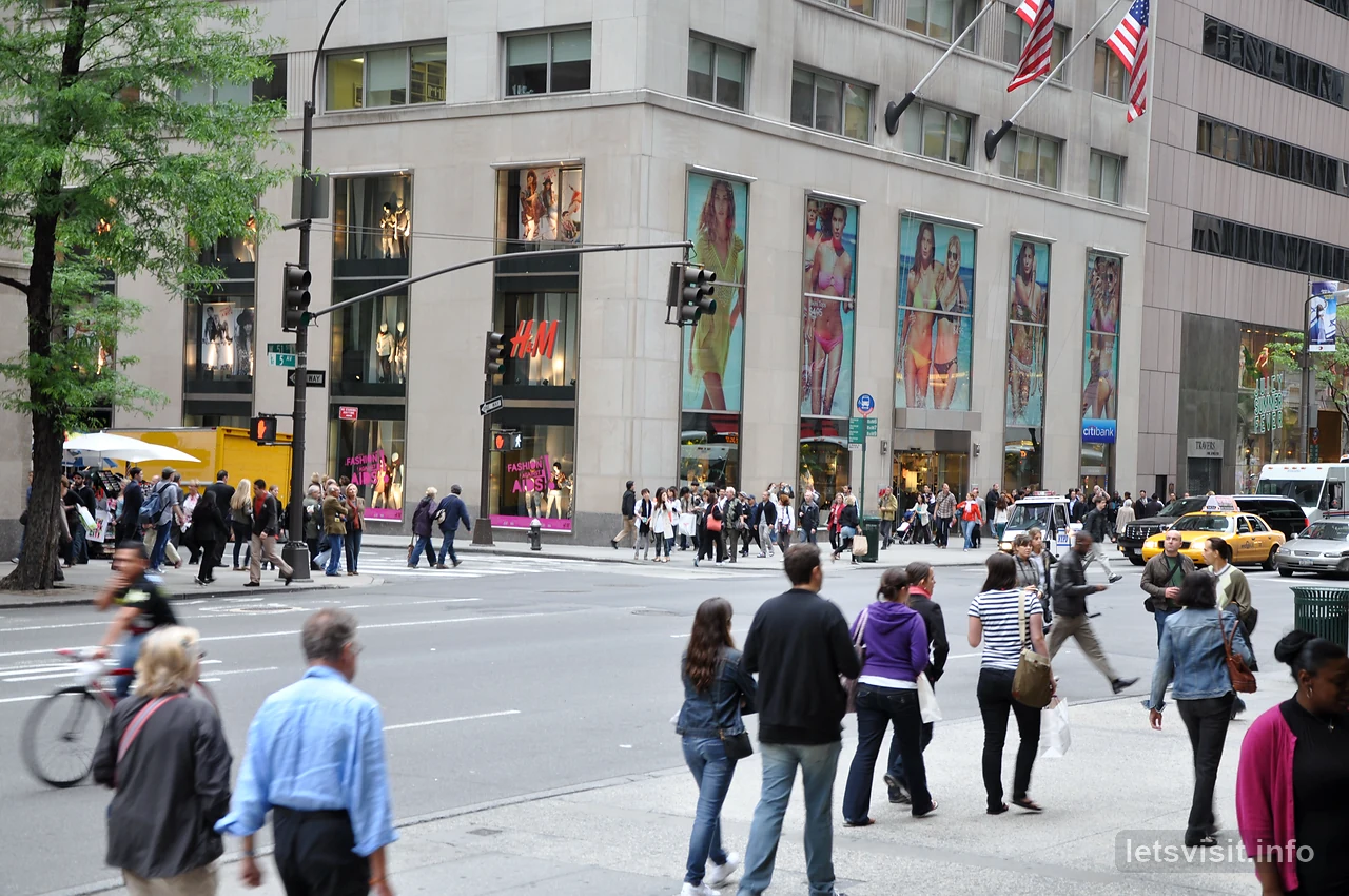 Pejalan kaki melintas Fifth Avenue bersebelahan kedai dan bendera
