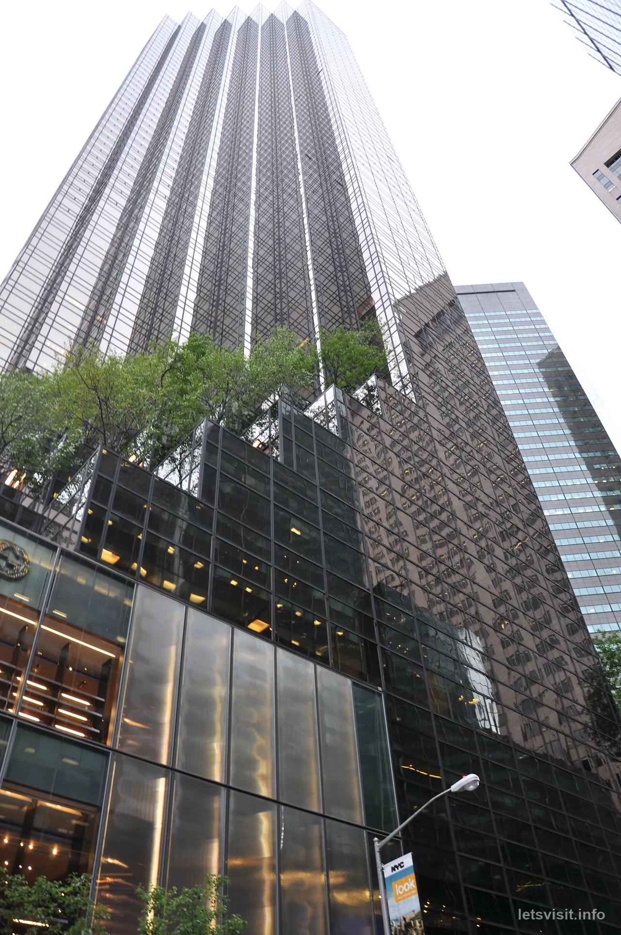 Fasad kaca Trump Tower menjulang di atas pokok di teres
