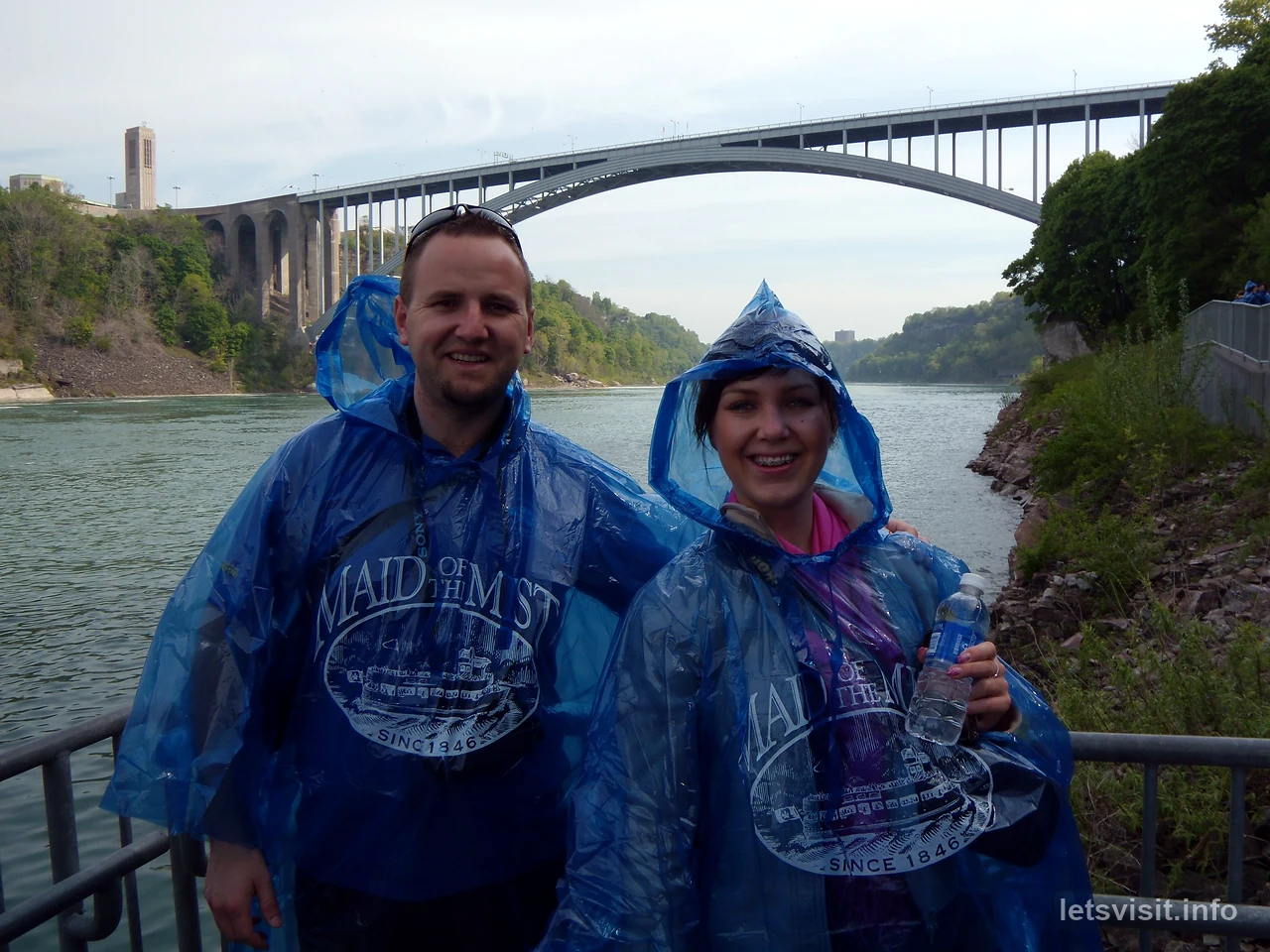 Dvoje putnika u plavim kabanicama s mostom Rainbow Bridge iza njih