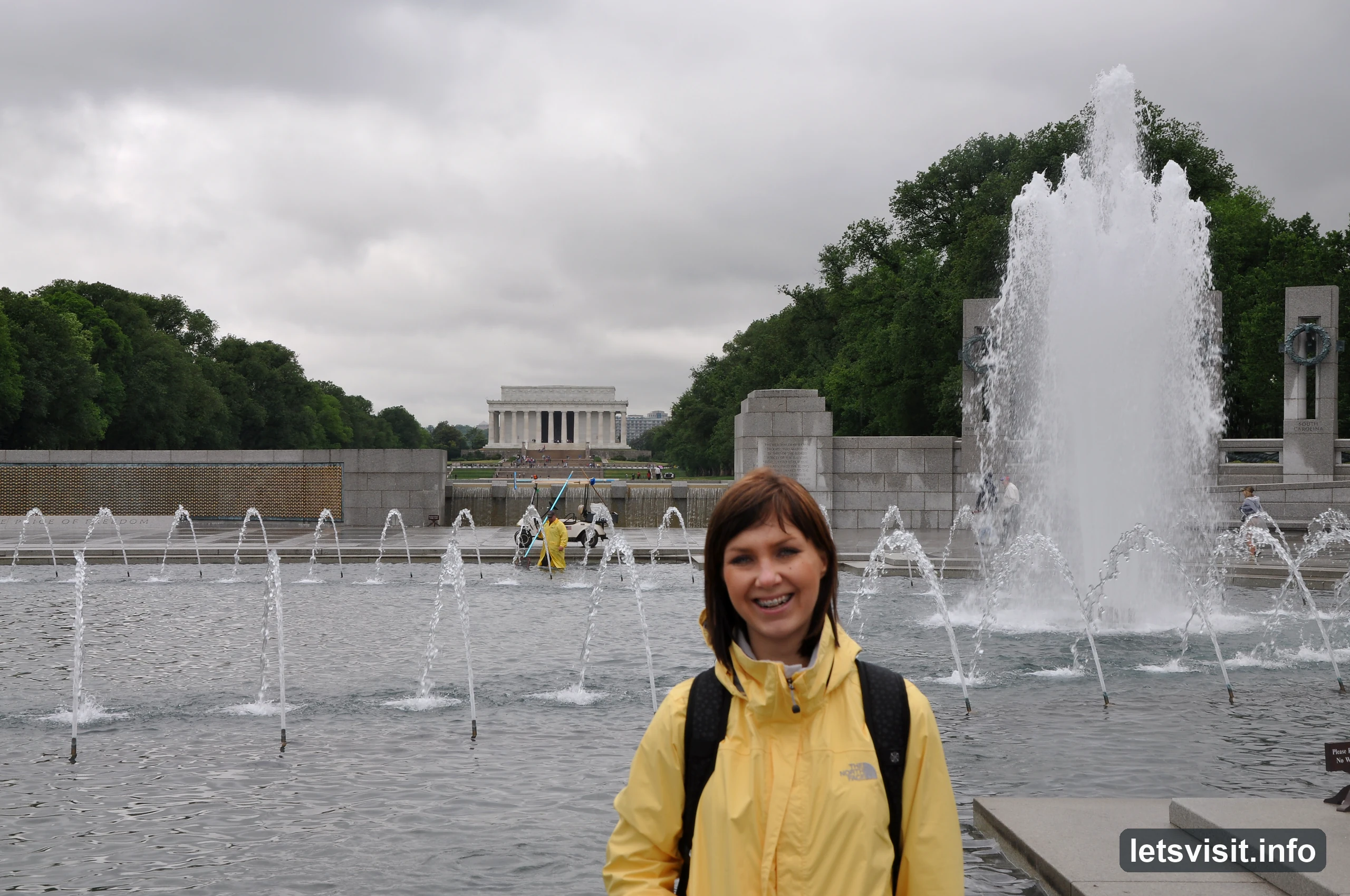 Traveller in a yellow rain jacket beside World War II Memorial fountains