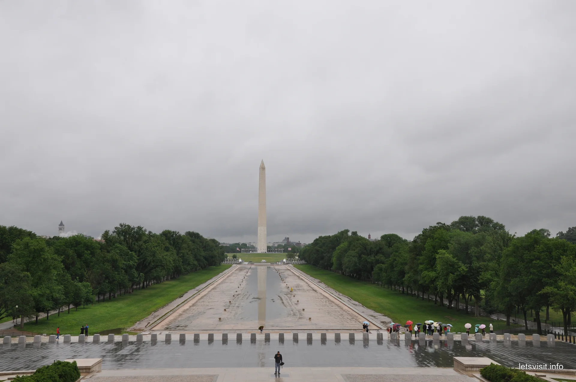 Washington Monument beyond the largely exposed Reflecting Pool basin, with umbrellas on wet paving