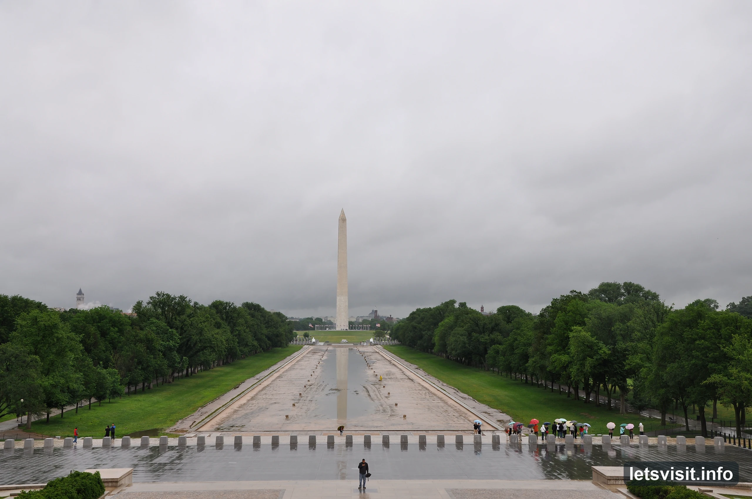 Washington Monument beyond the largely exposed Reflecting Pool basin, with umbrellas on wet paving