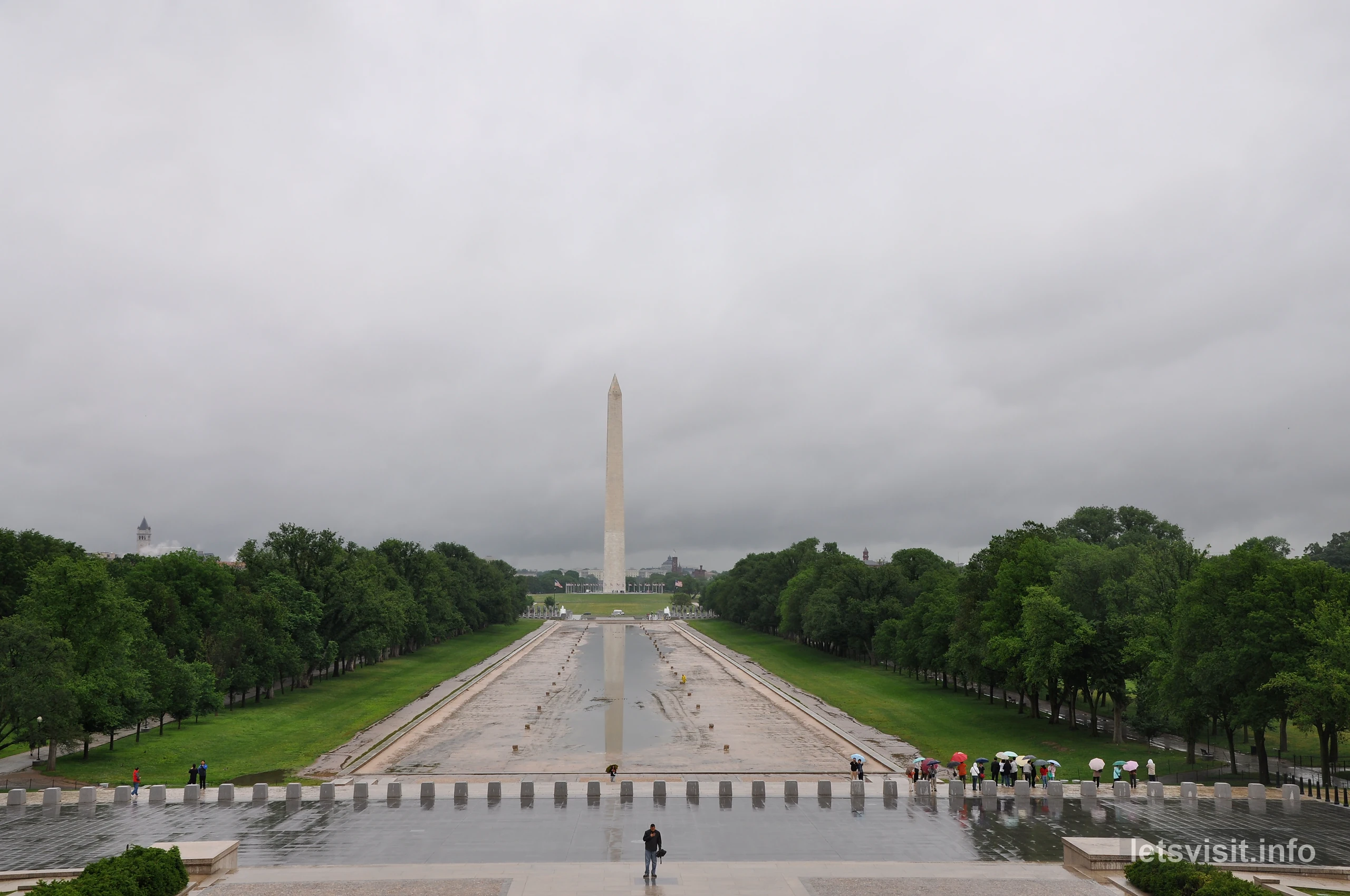 Washington Monument beyond the largely exposed Reflecting Pool basin, with umbrellas on wet paving