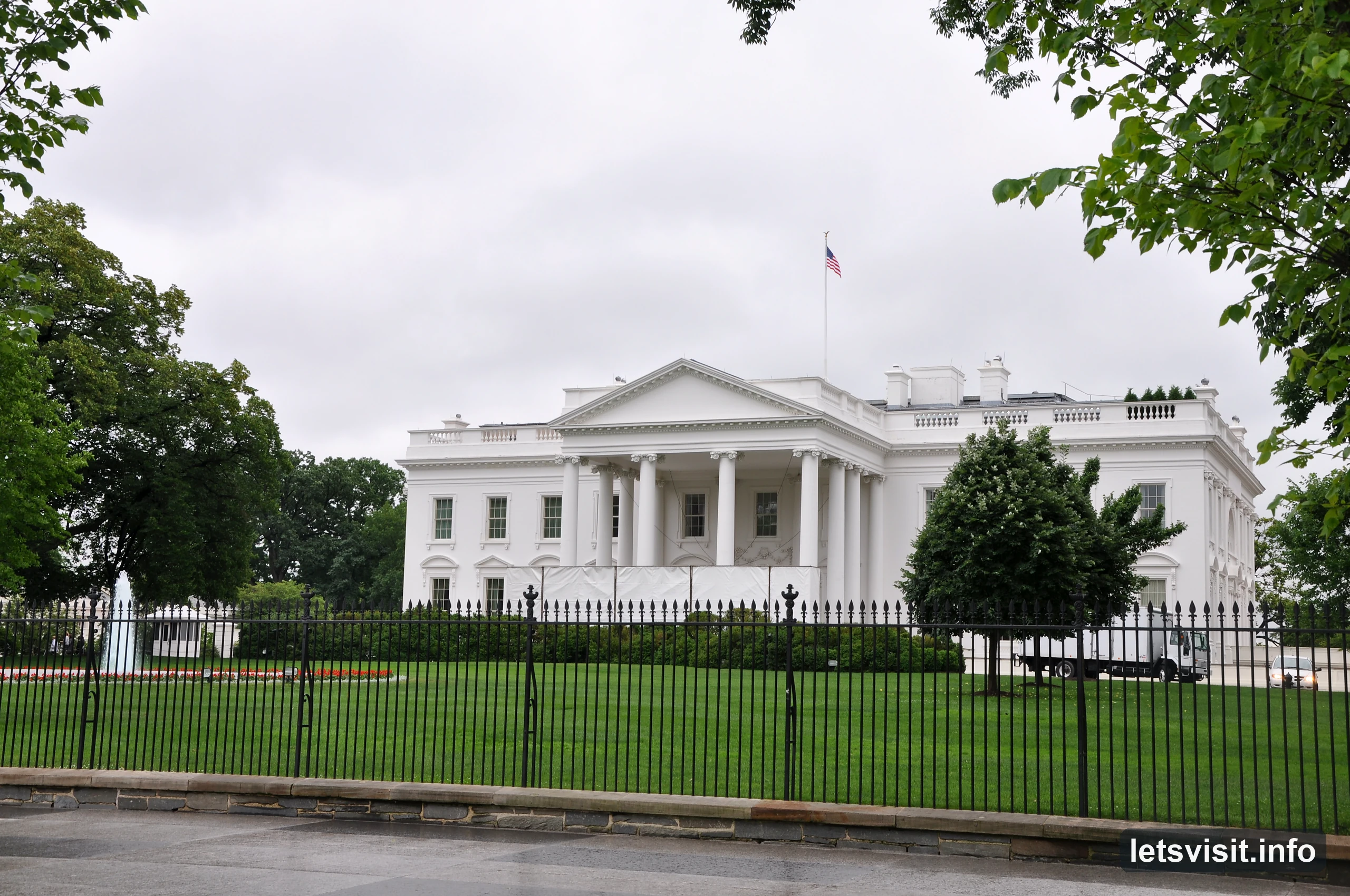 White House North Portico framed by leafy branches behind the black perimeter fence